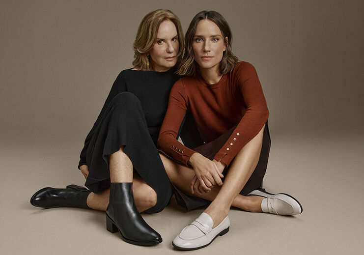 Duas mulheres sentadas exibindo sapatos elegantes.