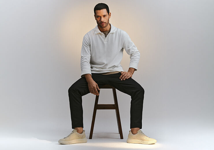 Homem sentado em banco, usando roupa casual clara