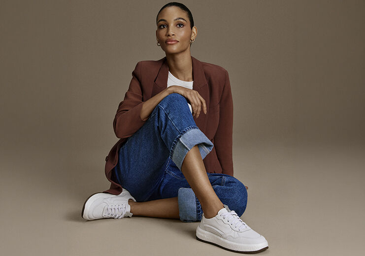 Modelo feminina com blazer e tênis sentado sobre o chão