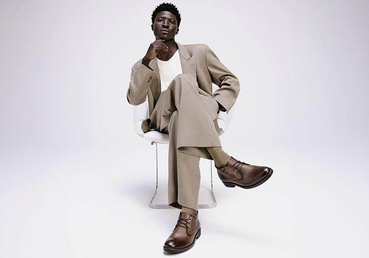 Homem em terno claro sentado com sapatos marrons.