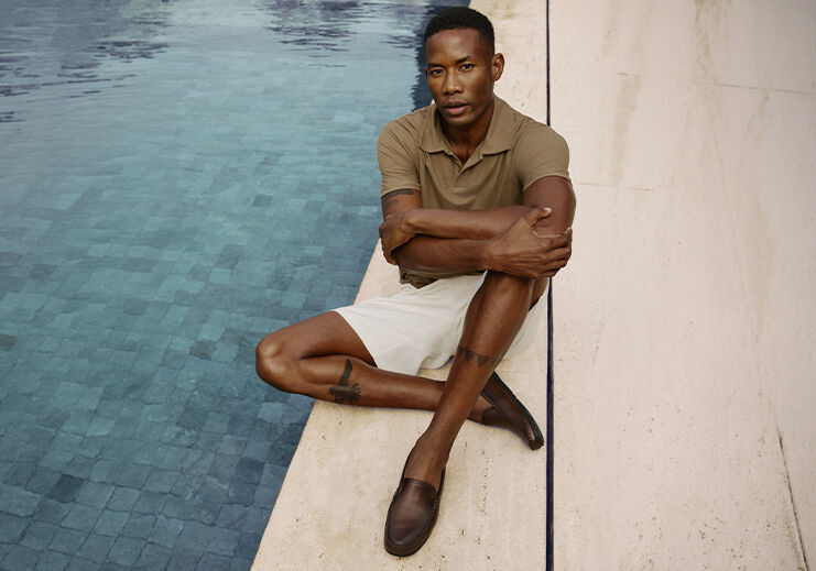 Homem relaxando à beira da piscina, com roupas casuais.