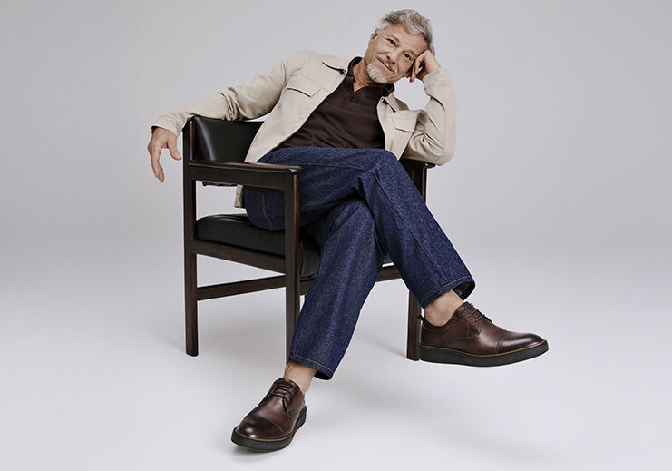 Homem sorridente sentado em cadeira com sapatos marrons